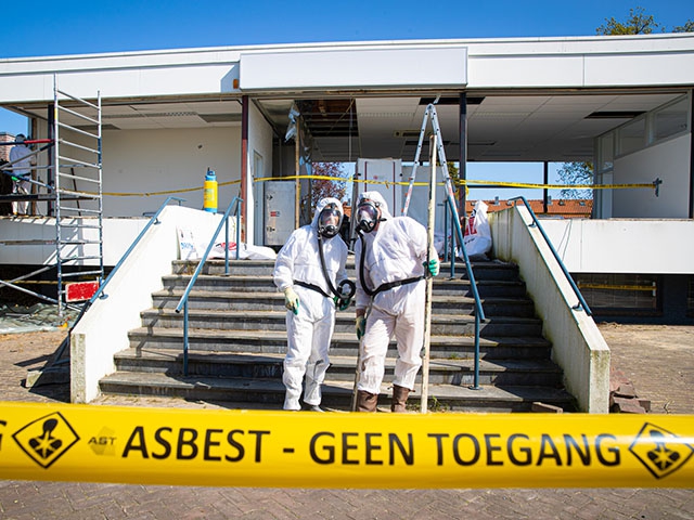 Saneerder in beschermende kleding verwijdert asbesthoudend materiaal in een afgeschermde ruimte