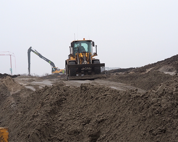 Wiellaadschop profileert een zandtalud op het werkterrein Havenkwartier bij mistig weer
