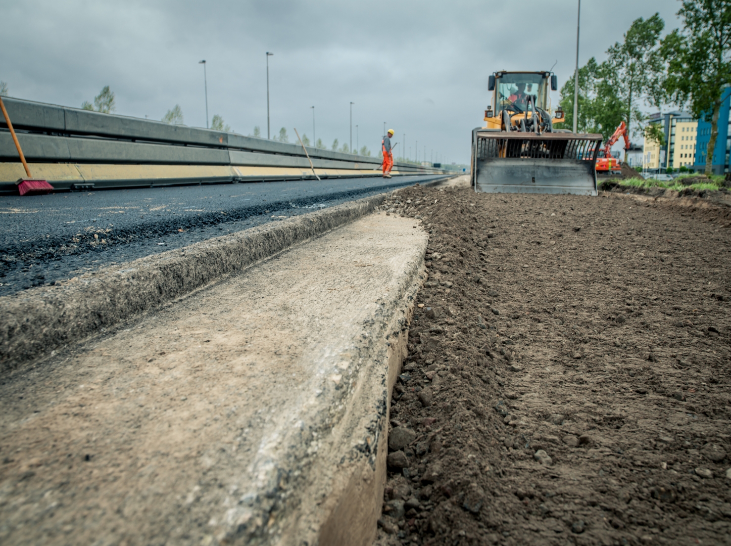 Vers aangelegde asfaltbaan met betonnen band, daarnaast een geëgaliseerde grondstrook waar een shovel aan het werk is