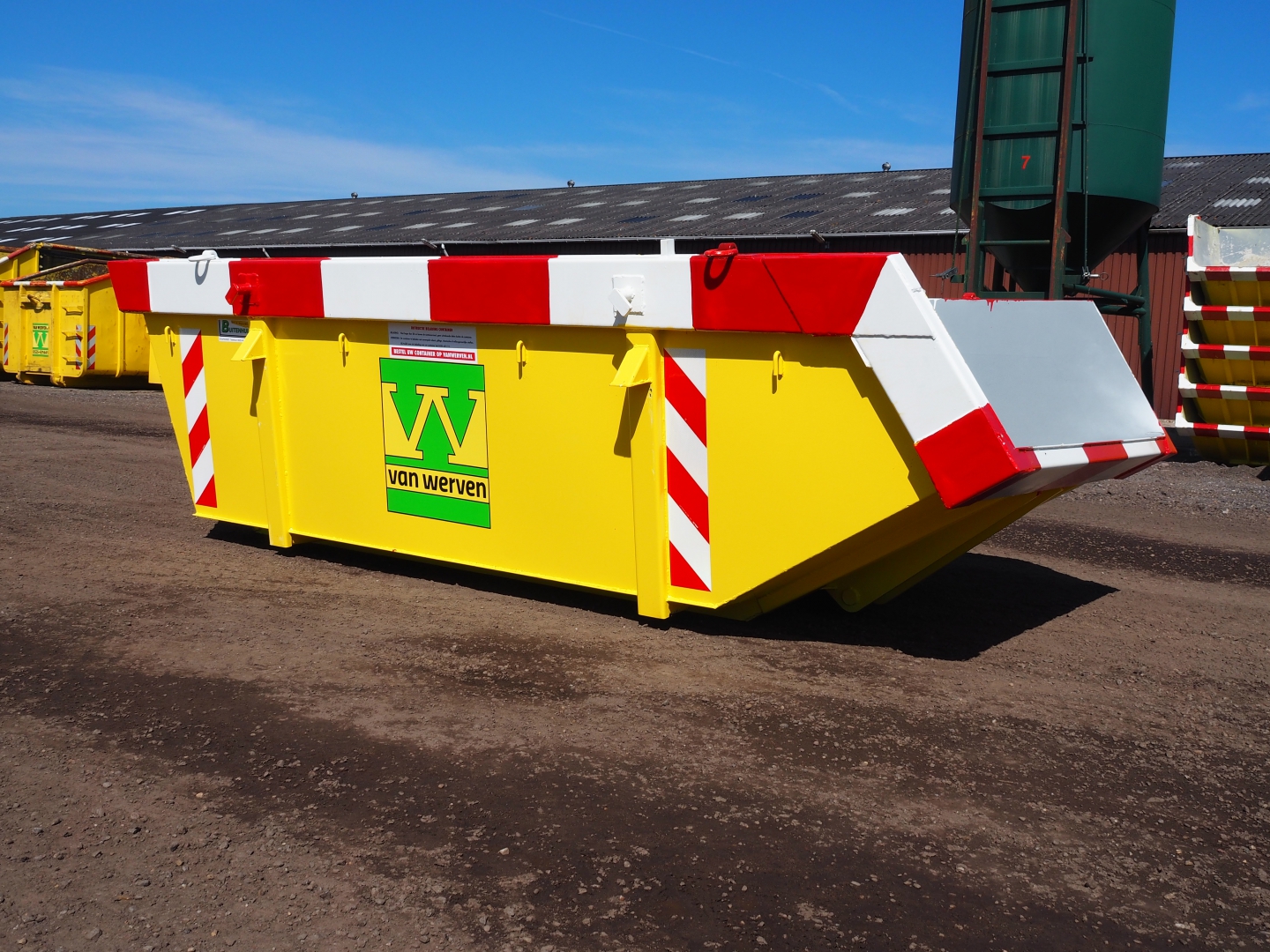 Gele afzetcontainer met rood-witte markering en Van Werven-logo, met geopende klep, op een bedrijfsterrein