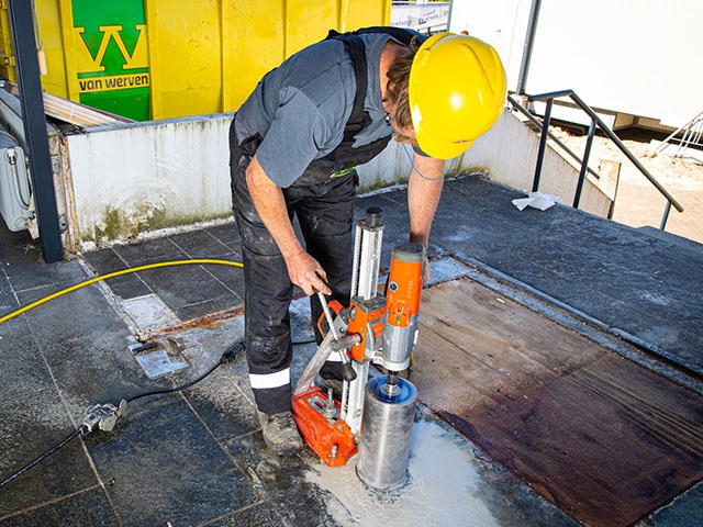 Medewerker boort met een kernboor een ronde opening in een betonnen wand