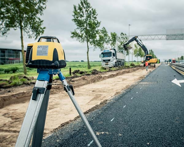 Bouwlaser op een statief langs een nieuw asfaltwegdek in aanleg