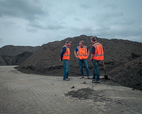 Drie medewerkers van Van Werven in oranje veiligheidsvest overleggen voor een lange berg compost op een recyclinglocatie