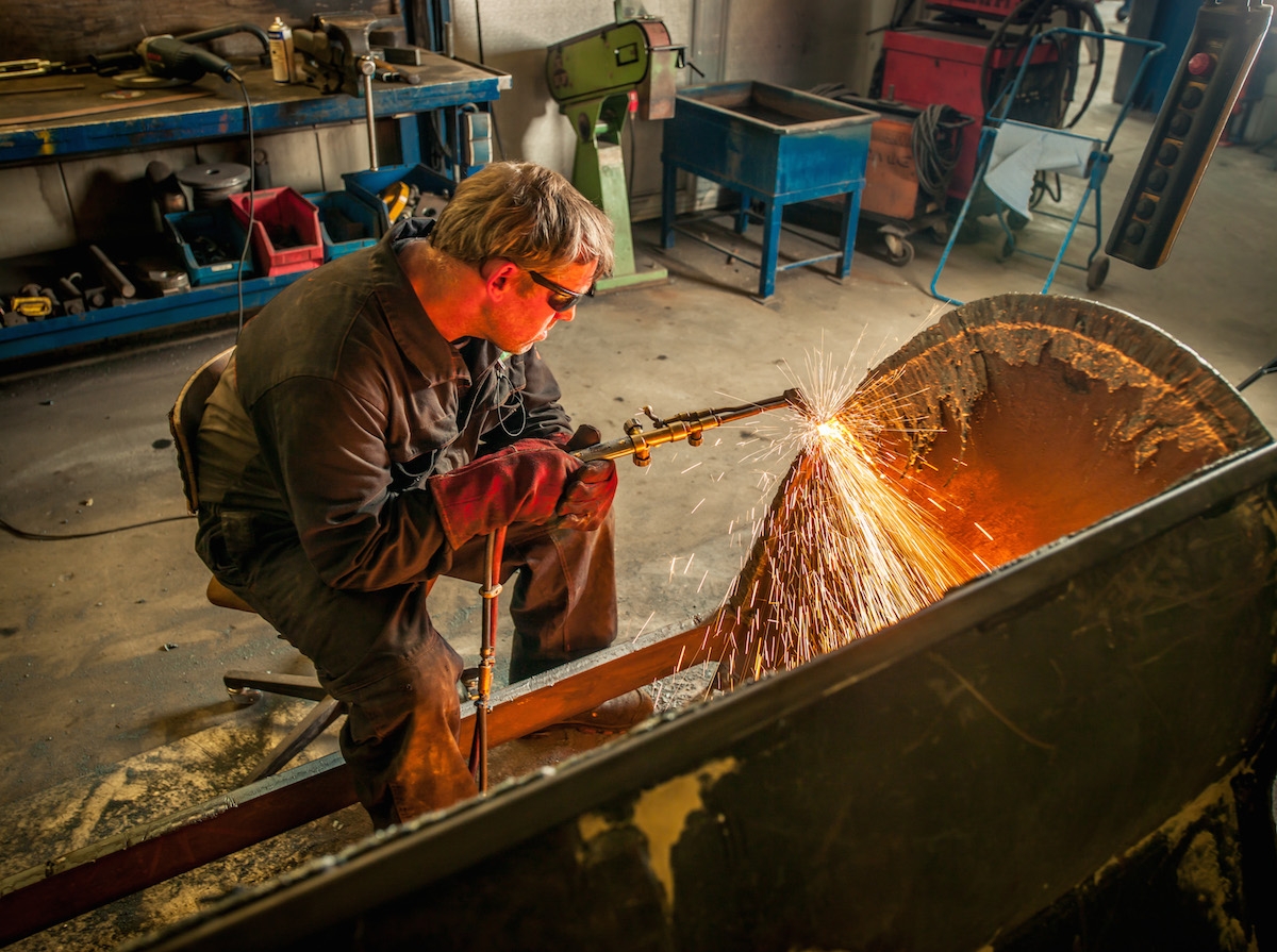Monteur snijdt met een snijbrander een graafbak bij, vonken spatten weg