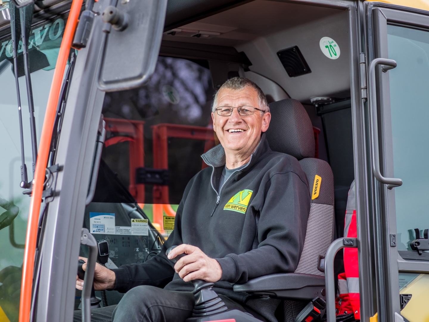 Machinist van Van Werven lacht vanuit de open cabine van zijn graafmachine