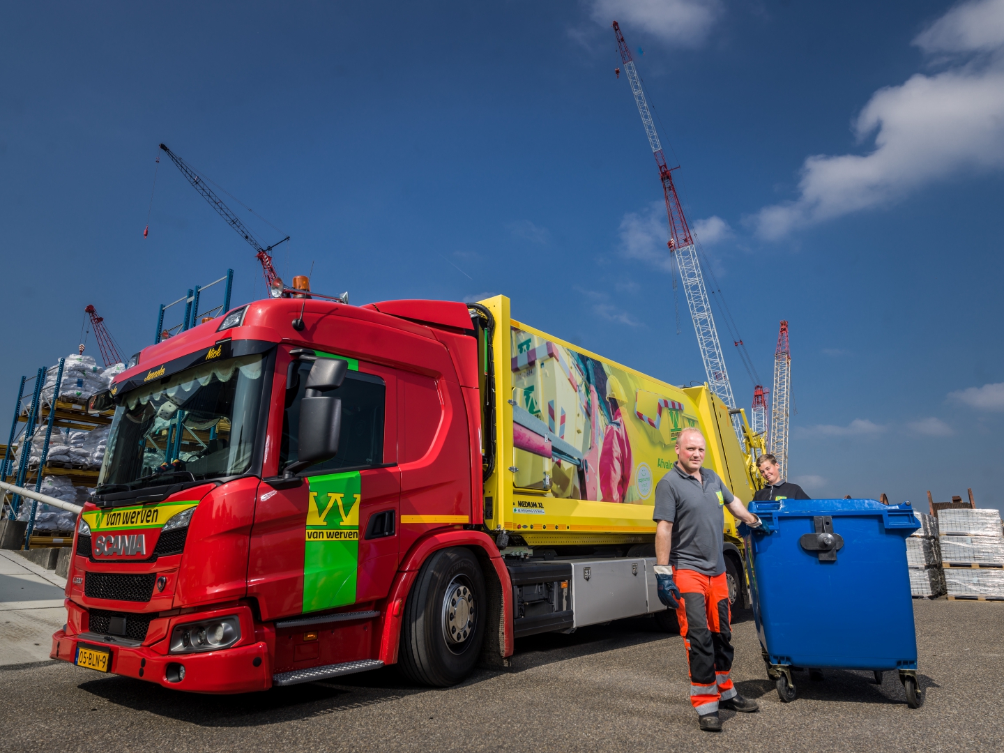 Twee medewerkers van Van Werven rollen een container naar een rood-gele inzamelwagen op een bouwplaats