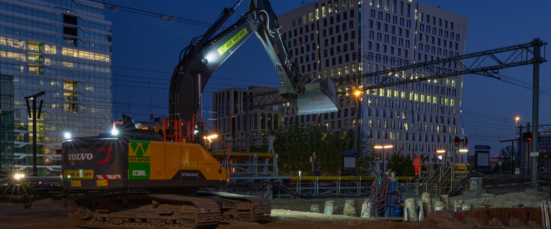 Rupskraan van Van Werven werkt bij avondlicht langs het spoor bij station Amsterdam Zuid