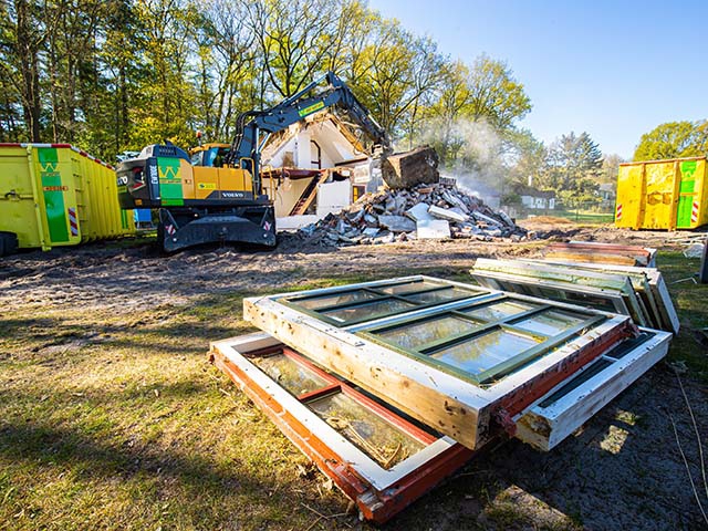 Gedemonteerde houten spanten en balken netjes gestapeld naast een pand in ontmanteling