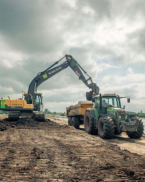 Rupskraan van Van Werven laadt grond in de kipper van een trekker op een werkterrein